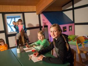 zwei Mädchen sitzen an einem Tisch in einem Raum mit einer Puppe in der Unterkunft Riekeshof in Schmallenberg