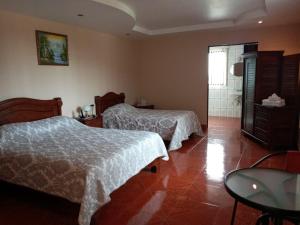 a bedroom with two beds and a table and a bathroom at Hotel Las Brumas in Cartago