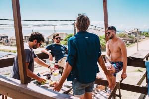 grupa mężczyzn stojących wokół stołu w obiekcie Mar de Fondo Hostel w mieście Punta del Diablo