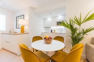 a white dining room with a white table and yellow chairs at Debambú Suites in Málaga