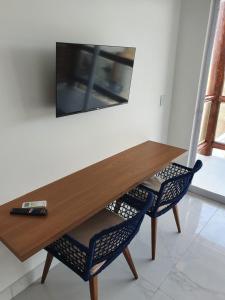 mesa de madera con 2 sillas y TV en la pared en Caly Pousada, en São Miguel do Gostoso