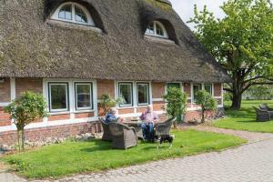 two people sitting in chairs in front of a house with a dog at Ferienwohnungen von Schassen in Twielenfleth