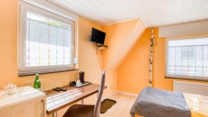 Zimmer mit orangefarbenen Wänden, einem Schreibtisch und einem Fenster in der Unterkunft Pension zum Rothaarsteig in Netphen