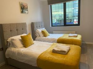 een slaapkamer met 2 bedden met gele lakens en een raam bij Zen Quality flats near Heathrow that are Cozy CIean Secure total of 8 flats group bookings available in Hounslow