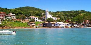 a boat in the water in front of a town at Pousada Maré Mar in Garopaba