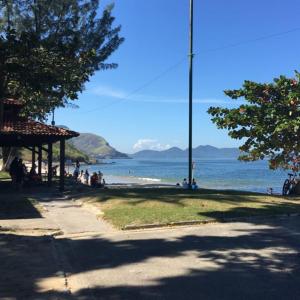 a group of people sitting on the grass near the beach at Sahy - Aldeia dos Reis, Condado - Apartamento Quarto e Sala in Mangaratiba