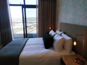 a bedroom with a bed with white pillows and a window at Menlyn Apartment in Pretoria