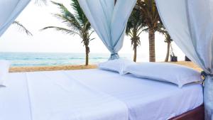 Grand-PopoMillenium Popo Beach Hotel的棕榈树和海洋海滩上的一张床位
