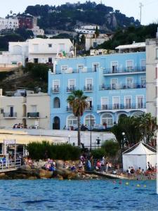 a blue building with people on the beach in front of the water at Relais Maresca Luxury Small Hotel & Terrace Restaurant in Capri