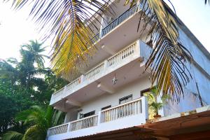 a white building with white balconies and palm trees at Omkar Sana Arambol in Arambol
