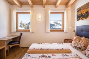 a bedroom with a bed and a desk and two windows at Ciasa Funtanies Sas dla Crusc in San Martino in Badia