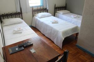 a room with two beds and a table with a remote control at Hotel Nossa Senhora Aparecida in Ouro Preto