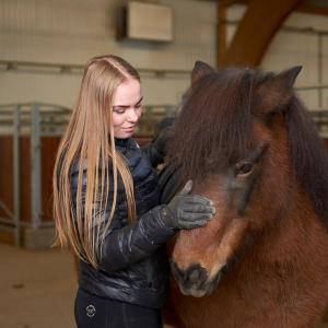 een vrouw die naast een bruin paard staat bij Syðra-Skörðugil Guesthouse in Varmahlid