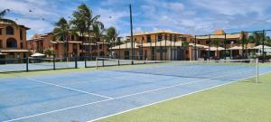 a tennis court with a net and some buildings at Condomínio PÉ NA AREIA no melhor de Guarajuba in Guarajuba