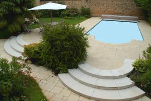 a swimming pool with stairs and an umbrella in a garden at La Demeure de l'Ile in Craon