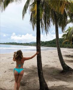 een vrouw in bikini die naast een palmboom op een strand staat bij CHEZ NOUS in Carrillo