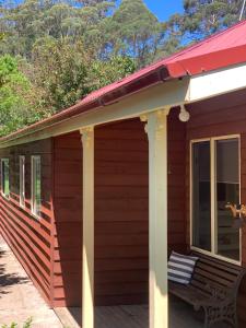 羅伯遜的住宿－Wallaby Cottage，红色小屋,门廊上设有长凳