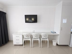 a white desk with two chairs and a tv on a wall at Casa Nostra Motel Mackay in Mackay