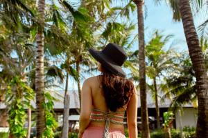 a woman wearing a hat standing in front of palm trees at Hotel Diễm My in Quy Nhon