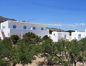 a group of white buildings on a beach with trees at Flora Apartments in Drios