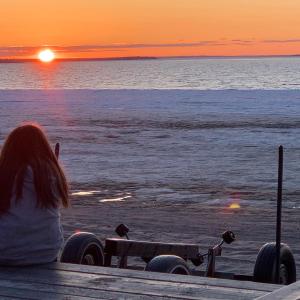 Uma mulher sentada numa doca a ver o pôr-do-sol. em Maison sur le lac em Desbiens