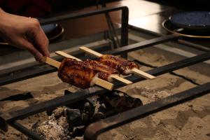 a person holding a skewer of meat on a grill at The Ninja Mansion in Toyota