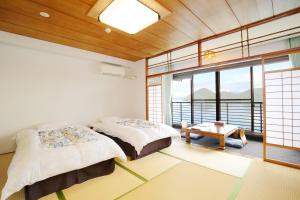 a bedroom with two beds and a table and windows at Toya-onsen Hotel Hanabi in Lake Toya