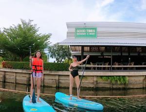 dos chicas están de pie en tablas de paddle en el agua en Good Times Resort -SHA Extra Plus, en Kanchanaburi