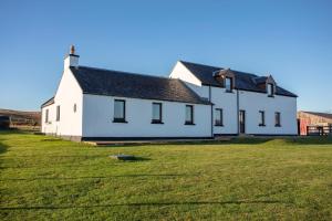 a white house with a grassy field in front of it at Kentraw Farmhouse Luxury Self Catering in Bruichladdich