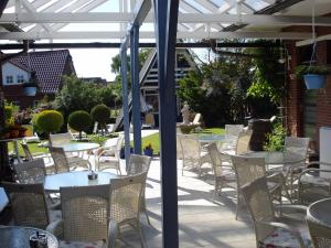 a patio with tables and chairs under a white pergola at Hotel Zur Fischerklause in Fedderwardersiel