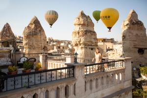 a woman standing on a balcony with hot air balloons at Stone House Cave Hotel in Goreme