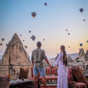 un hombre y una mujer de pie en un balcón con globos de aire caliente en Elite Cave Suites en Göreme