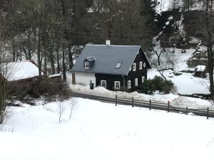 Ein schwarzes Haus im Schnee mit einem Zaun in der Unterkunft Chalupa Rozmarýna in Mařenice