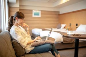 a woman sitting on a couch with a laptop in a hotel room at Niigata Grand Hotel in Niigata