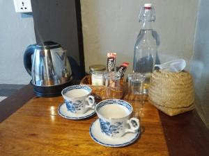 two cups of coffee on a wooden table with a bottle at Khmer Hands in Kep