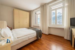 a bedroom with a bed and a tv and two windows at Hotel Marcora & Spa in San Vito di Cadore