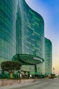 un grand bâtiment en verre avec un panneau devant lui dans l'établissement Millennium Al Rawdah Hotel, à Abu Dhabi