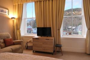 a bedroom with a tv on a dresser in front of windows at The Gordon Guest House in Ballater