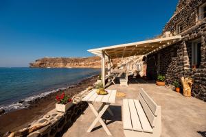 a patio with a table and benches next to the water at BLACK BAY CAVES SUITES in Akrotiri