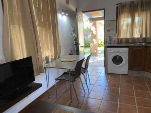 uma cozinha com uma mesa, uma televisão e uma máquina de lavar roupa em Casita con jardín privado y piscina compartida em Cádiz