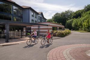 two women riding bikes down a street in front of a building at Hôtel du Golf in Lumbres