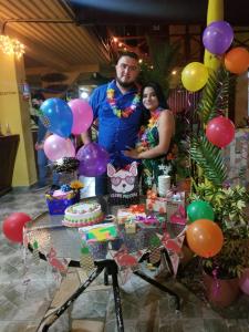 a man and a woman standing next to a table with a cake and balloons at Hotel BAH&Iacute;A in Tela