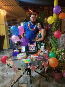 a man and a woman standing next to a table with a cake and balloons at Hotel BAHÍA in Tela