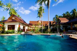 a swimming pool in front of a house with palm trees at Kanok Buri Resort in Lipa Noi