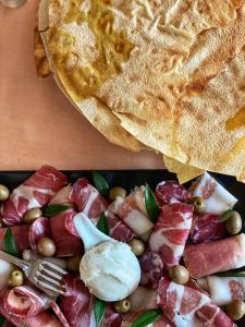 a plate of food with ham and cheese and a tortilla at Locanda Tipica Sa Corte in Oliena