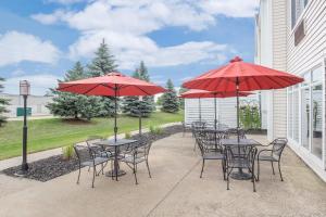 eine Terrasse mit Tischen, Stühlen und roten Sonnenschirmen in der Unterkunft Cobblestone Suites - Oshkosh in Oshkosh