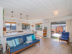 a living room with a blue couch and a kitchen at Shore Beats Work - Whangamata Holiday Home in Whangamata