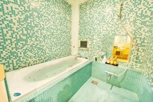 a bathroom with a tub and a tiled wall at Nagasaki Chapel Coconuts Hotel ＆Resort in Isahaya