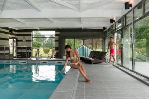 a woman in a bikini sitting on the edge of a swimming pool at Hôtel Château Tilques in Tilques