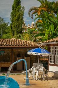 a pool with two chairs and an umbrella and a fountain at Pousada Chafariz das 4 Estações in Tiradentes